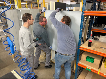 Drei Mitarbeiter gestalten gemeinsam eine Materialtafel im Arbeitsbereich